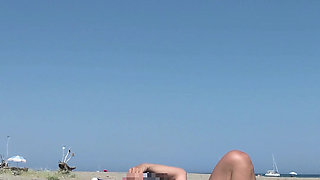 She masturbates her on the naturist beach in public with a voyeur who passes by